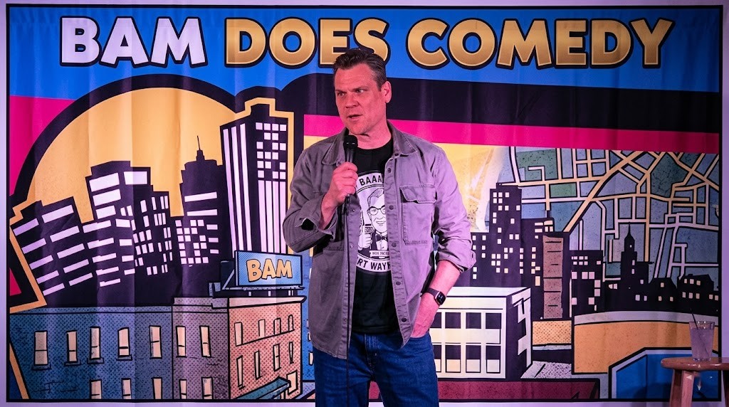 Bam performing stand-up in front of the Bam Does Comedy backdrop